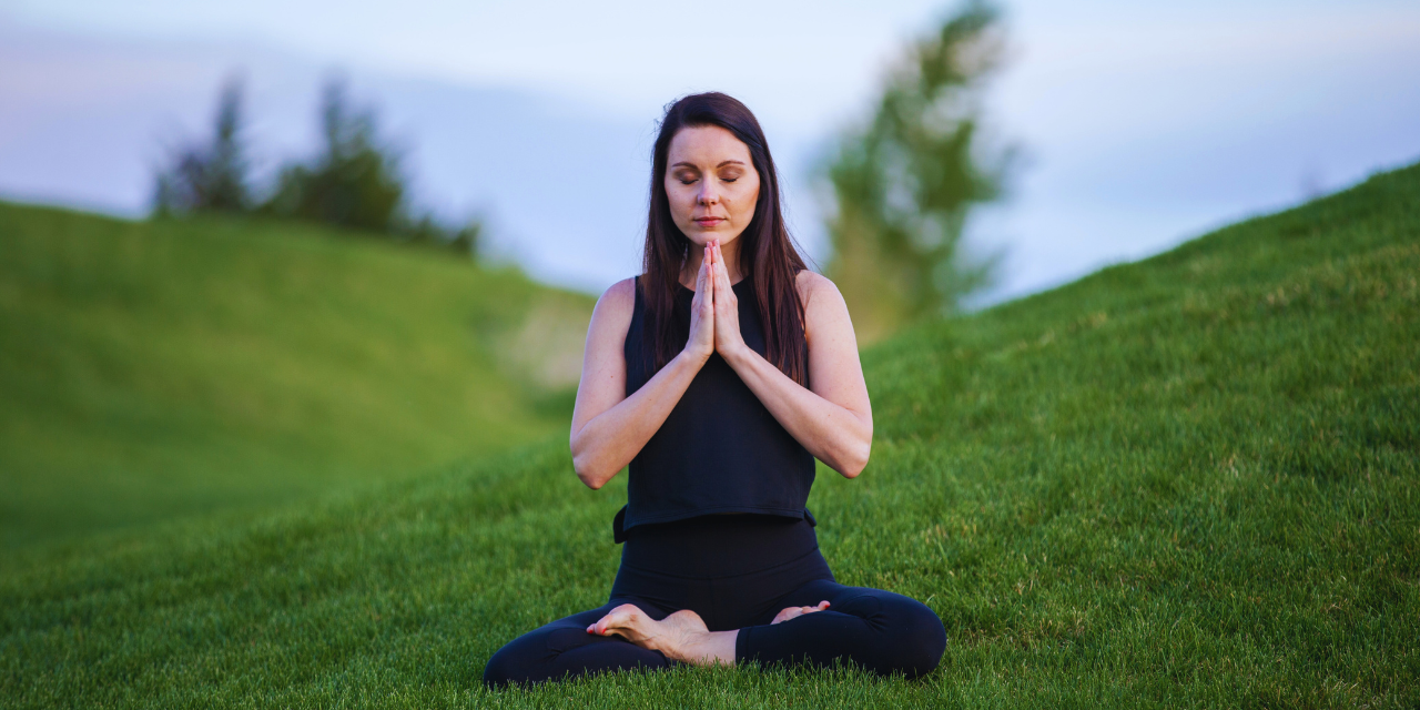 a lady meditating by sitting on grass